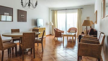Ein geräumiges Wohnzimmer mit Essbereich, Korbmöbeln, einer Kronleuchter und einem Fernseher.
