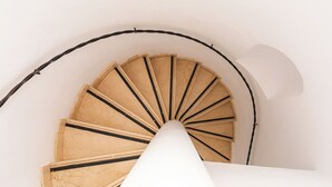 Una scala a chiocciola con gradini in legno e corrimano nero, che sale in una stanza dalle pareti bianche.