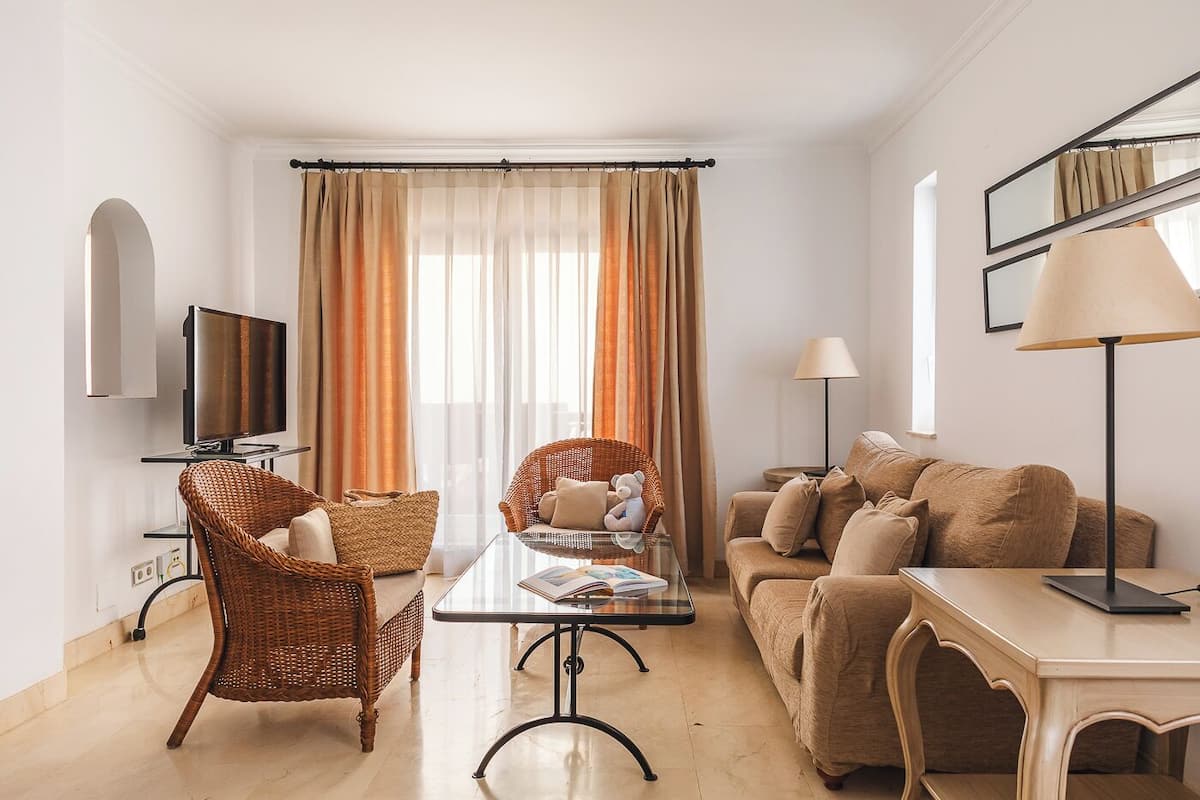 Ein Wohnzimmer mit Fernseher, Korbsesseln, einer Couch, einem Tisch und einer Lampe.