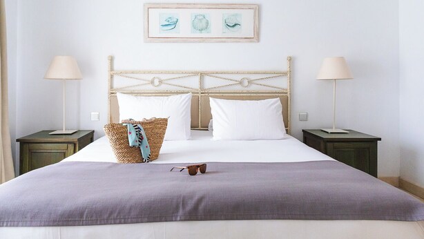 Un letto rifatto con cura, una testiera, due comodini e un quadro incorniciato sopra il letto.