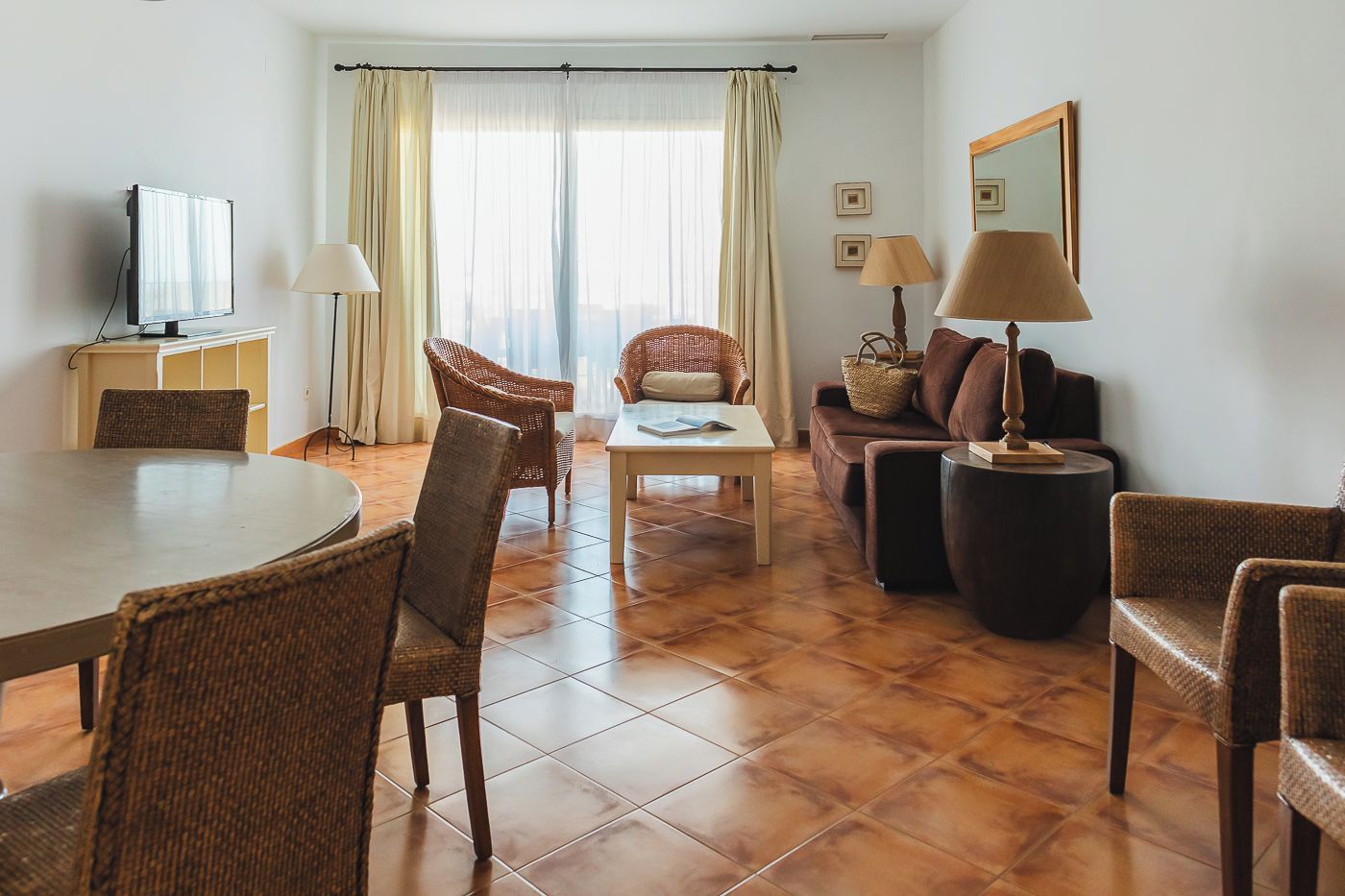 Ein Hotelzimmer mit Esstisch, Stühlen, einer Couch, einem Fernseher und einem Fenster mit Vorhängen.