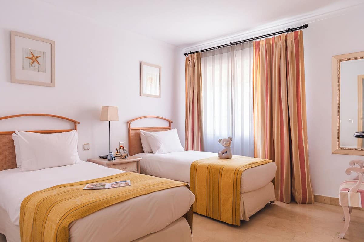 Ein Hotelzimmer mit zwei Betten, einem Nachttisch mit Lampe, einem Teddybären und einer Meerstern-Dekoration.