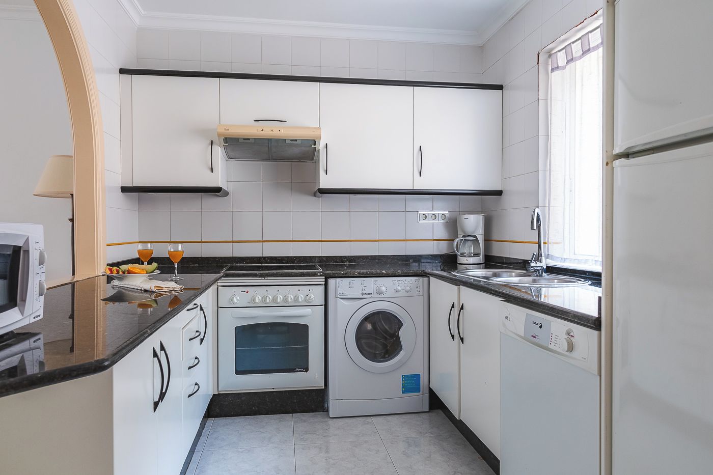 A compact kitchen with a stove, oven, washing machine, and a coffee maker.
