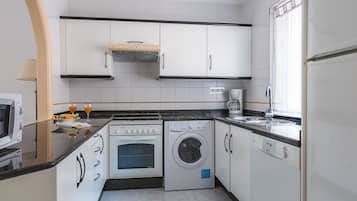 A compact kitchen with a stove, oven, washing machine, and a coffee maker.