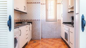 A compact kitchen with white cabinets, a washing machine, a stove, and a window providing natural light. - Ona Las Lomas Village (Cartagena)