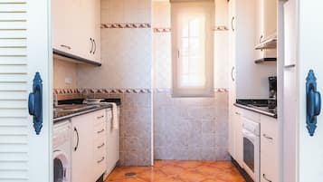 Una cuina compacta amb armaris blancs, una rentadora, una placa de cocció i una finestra que aporta llum natural.