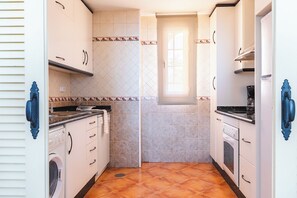 Una cuina compacta amb armaris blancs, una rentadora, una placa de cocció i una finestra que aporta llum natural.