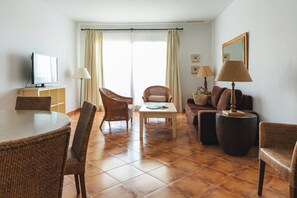 A living room with a dining area, wicker furniture, a television, and a large window with curtains. - Ona Las Lomas Village (Cartagena)