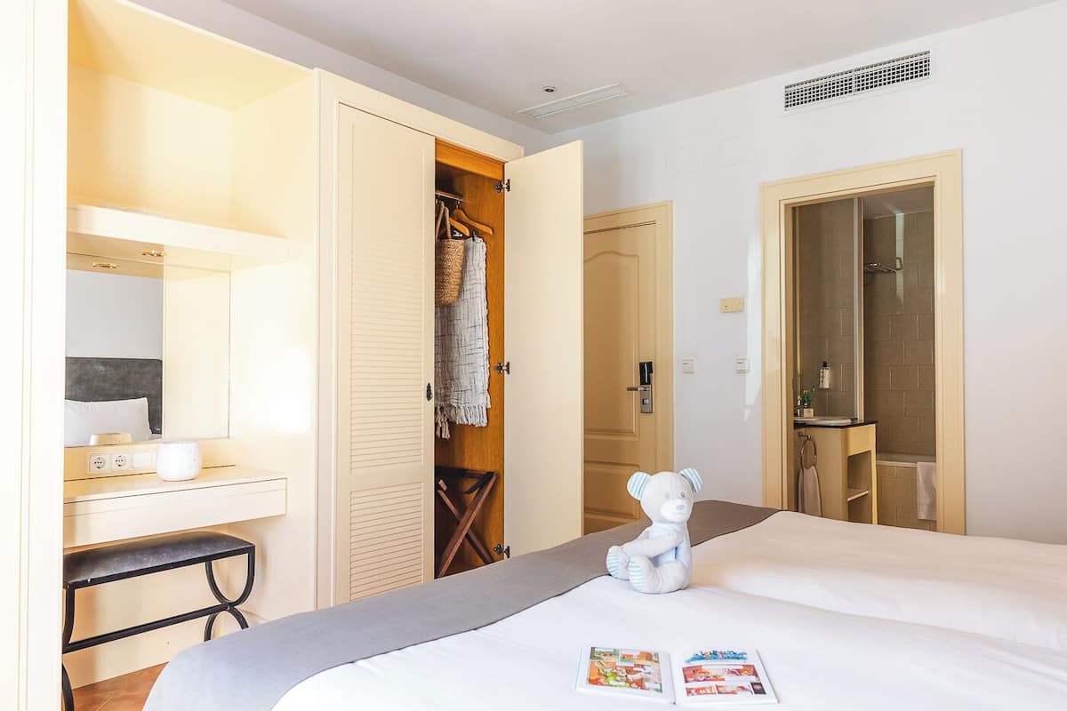 Ein Hotelzimmer mit einem Bett, einem Schreibtisch mit Lampe, einem Kleiderschrank und einem Badezimmer mit Dusche und Spiegel.