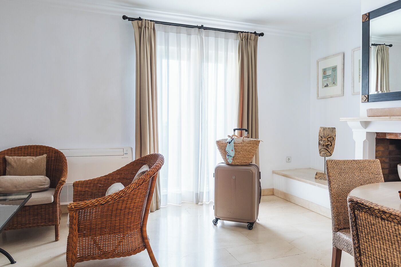 A hotel room with wicker furniture, a fireplace, and a view of the outdoors.