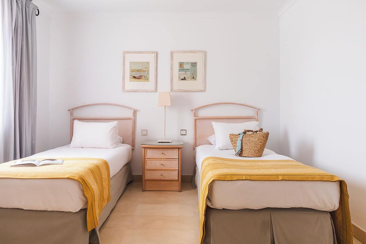 Ein Hotelzimmer mit zwei Einzelbetten, einem Nachttisch, einer Lampe und zwei gerahmten Bildern an der Wand.