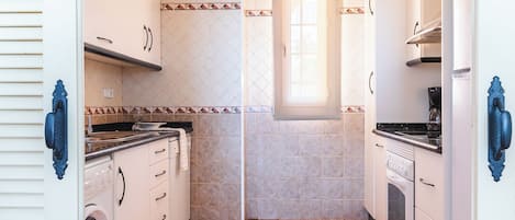 A compact kitchen with white cabinets, a washing machine, a stove, and a window providing natural light.