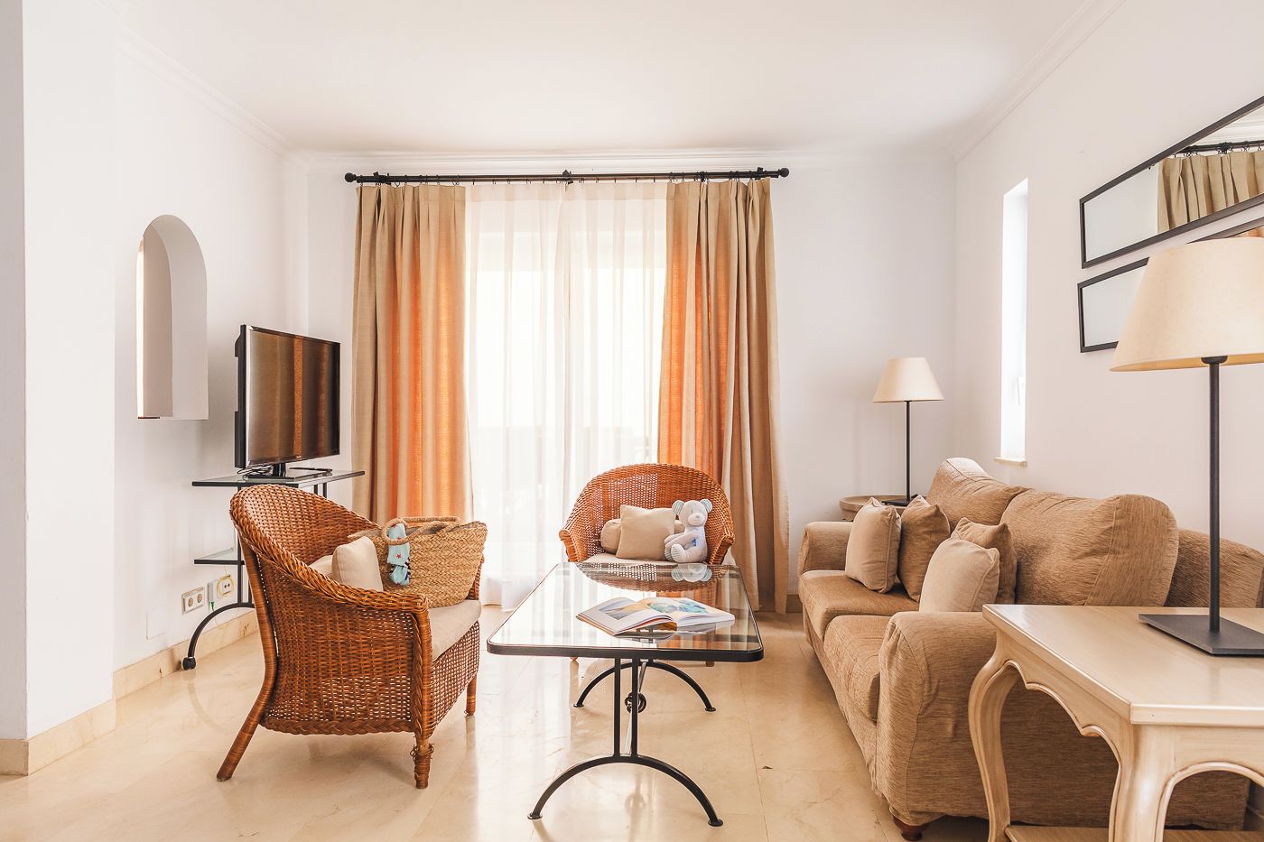 Ein modernes Wohnzimmer mit Fernseher, Korbstühlen, einem Glastisch und einer Couch.