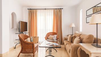Ein modernes Wohnzimmer mit Fernseher, Korbstühlen, einem Glastisch und einer Couch.