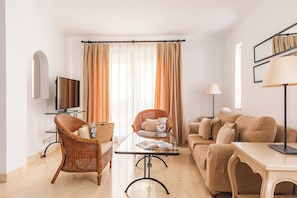 A modern living room with a television, wicker chairs, a glass coffee table, and a sofa. - Ona Las Lomas Village (Cartagena)