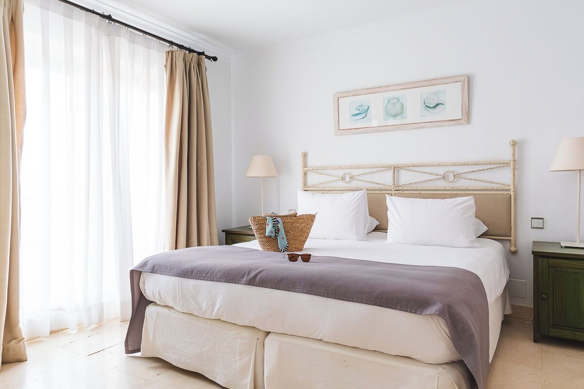 Una camera da letto ordinata con un letto, comodini, una lampada e un quadro appeso al muro.
