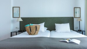 A neatly made bed with white pillows and a grey bedspread, a wicker basket with towels, and a book on the bed. - Ona Las Lomas Village (Cartagena)