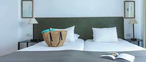 Una cama bien hecha con almohadas blancas y una colcha gris, una cesta de mimbre con toallas y un libro sobre la cama.