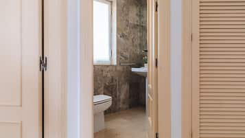 Ein schmaler Flur, der zu einem Badezimmer mit Toilette, Fenster und Waschbecken führt.