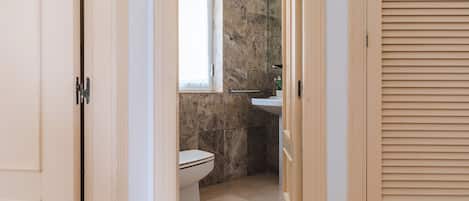 Un pasillo estrecho que conduce a un baño con inodoro, ventana y lavamanos.