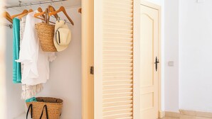 Armadio a muro con porta in legno, appendiabiti con vestiti e cesti, e pavimento piastrellato.