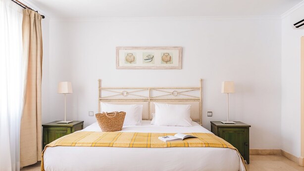A neatly arranged bedroom with a bed, two bedside tables, a headboard, and a framed picture on the wall. - Ona Las Lomas Village (Cartagena)