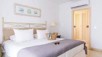 Een netjes opgemaakte slaapkamer met een bed, een bedlampje, een mand met handdoeken en een ingelijste foto aan de muur.