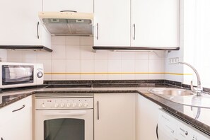 Cuina amb armaris blancs, microones, forn i rentavaixelles.