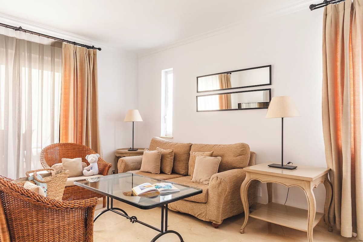 Ein modernes Wohnzimmer mit einem beigefarbenen Sofa, einem Glastisch, einem Korbstuhl und zwei Stehlampen.