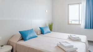 Una habitación de hotel con dos camas, una mesita de noche pequeña, una planta en maceta y una ventana con cortinas.