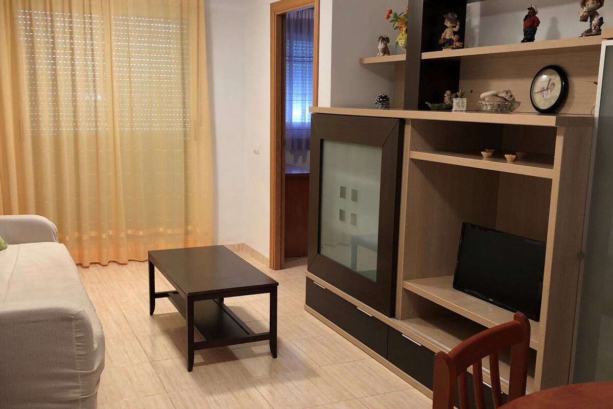 A modern living room with a sofa, a coffee table, a TV, and a wooden entertainment unit with figurines.