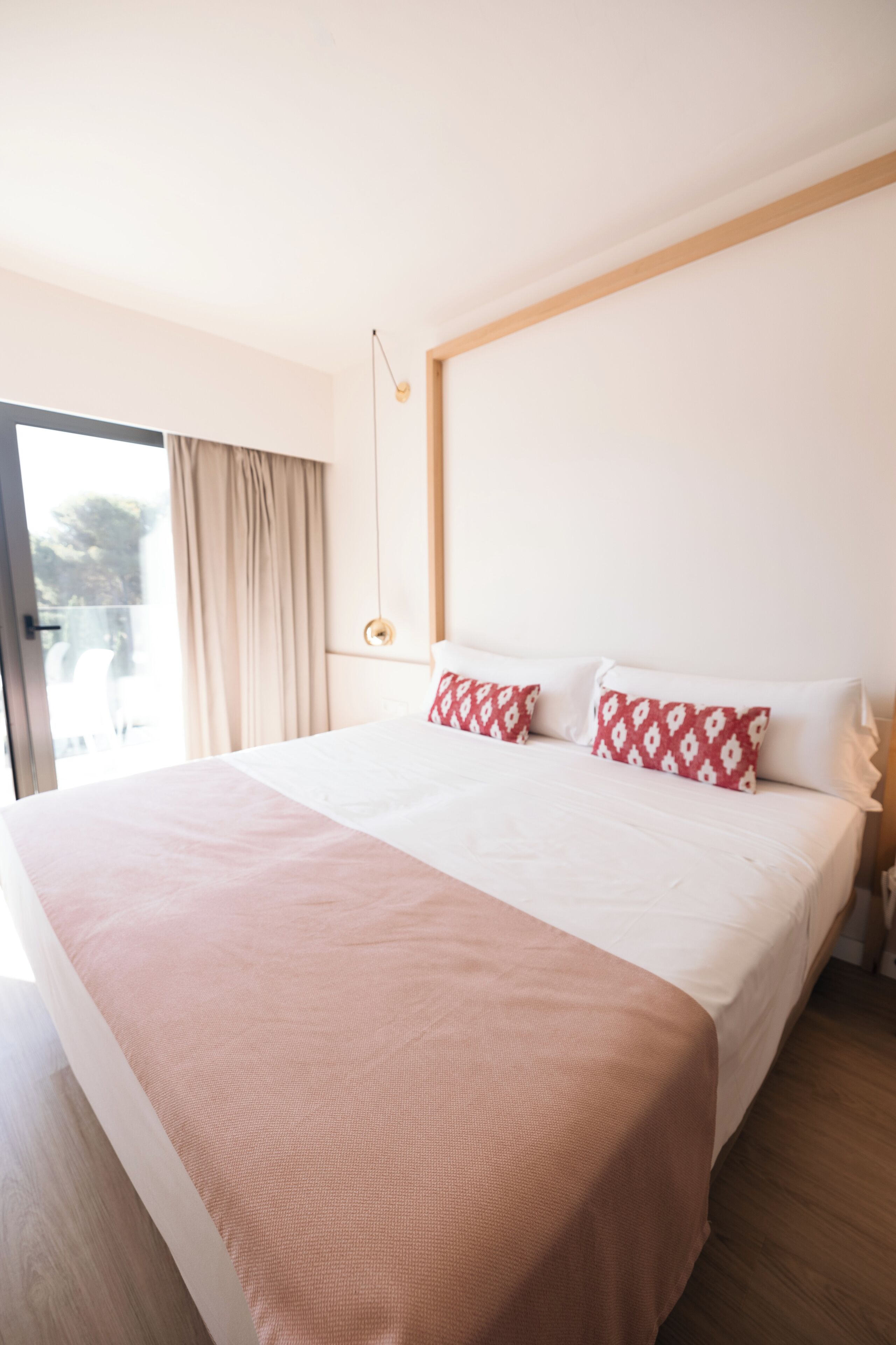 Una cama grande con una colcha rosa, almohadas blancas y un cabecero de madera.