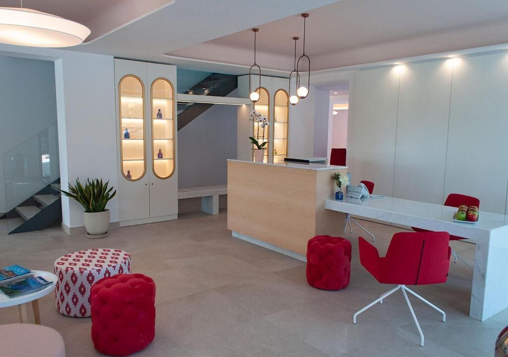 Un moderno vestíbulo de hotel con una recepción, sillas rojas, una escalera y una planta en maceta.