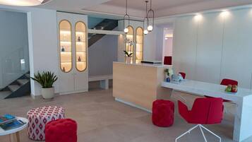 Un moderno vestíbulo de hotel con una recepción, sillas rojas, una escalera y una planta en maceta.
