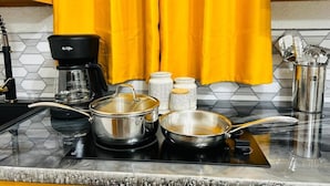 Eine Küche mit einer Kaffeemaschine, Töpfen, einer Pfanne und Gewürzbehältern auf einer Arbeitsplatte.