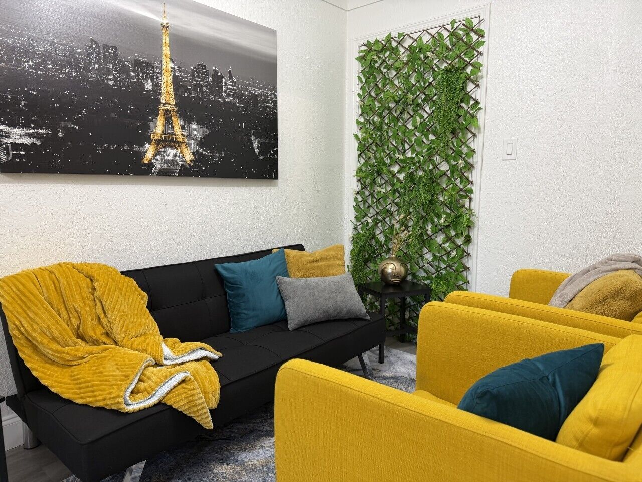 Un salon avec un canapé noir, des fauteuils jaunes et un jardin vertical vert.