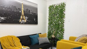 Una sala de estar con un sofá negro, sillones amarillos y un jardín vertical verde.