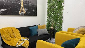 Un salon avec un canapé noir, des fauteuils jaunes et un jardin vertical vert.
