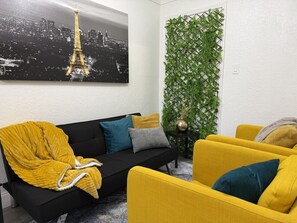 Ein Wohnzimmer mit einer schwarzen Couch, gelben Sessel und einer vertikalen grünen Wandbegrünung.