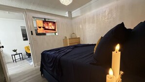 Un dormitorio con cama, una araña y una vela encendida sobre una mesita de noche.