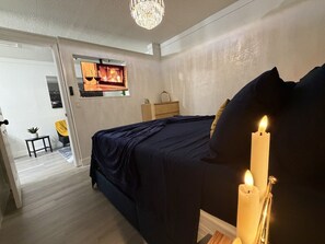 Ein Schlafzimmer mit einem Bett, einer Chandelierleuchtre und einer brennenden Kerze auf einem Nachttisch.