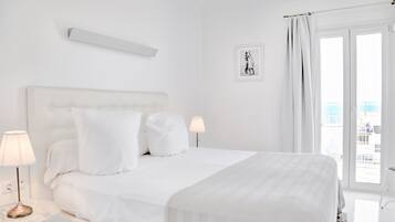 Habitación de hotel con una cama grande, dos lámparas de noche, un cuadro en la pared y vista al mar por la ventana.
