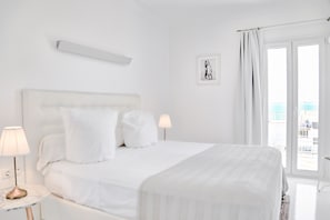 Habitación de hotel con una cama grande, dos lámparas de noche, un cuadro en la pared y vista al mar por la ventana.