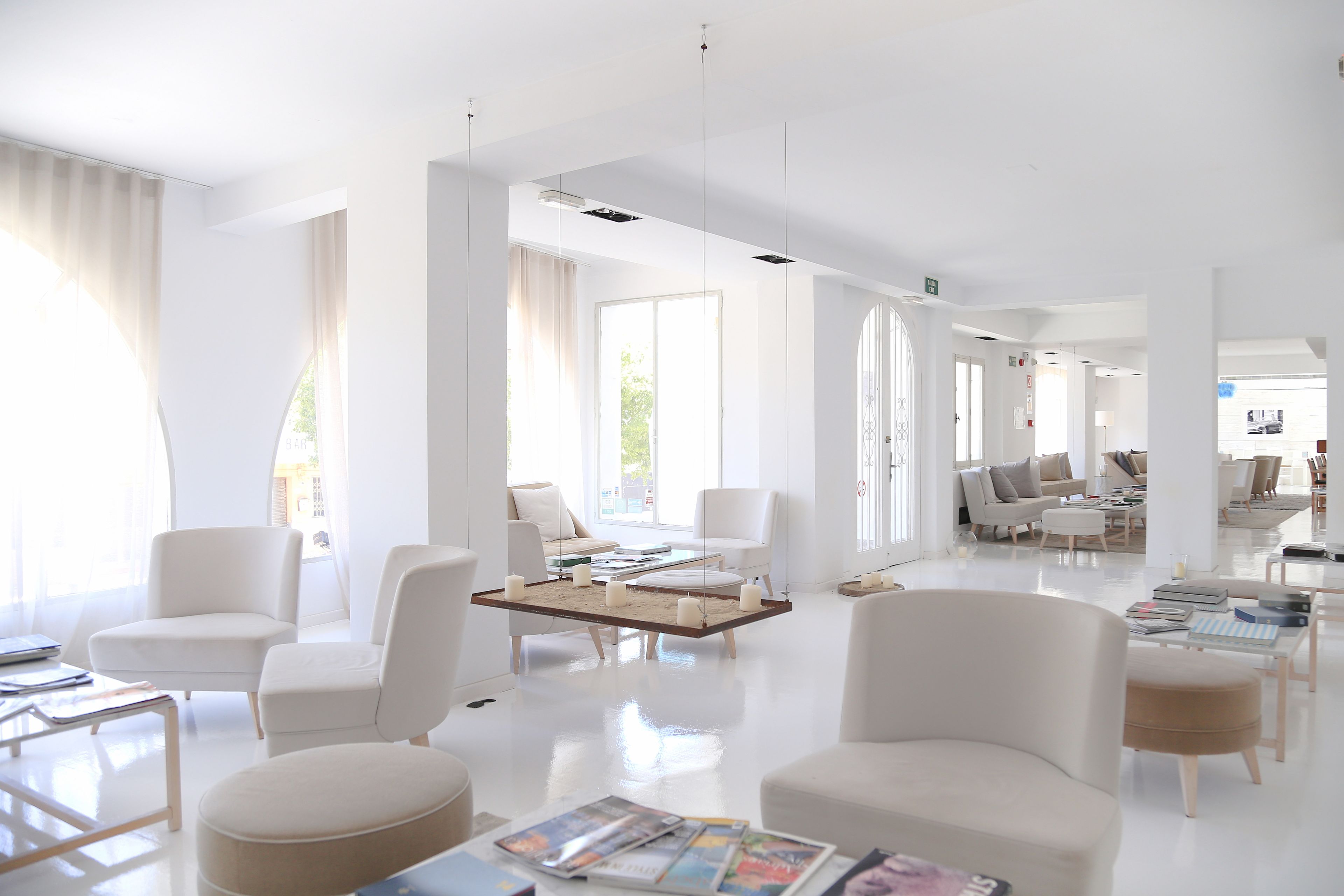 En rummelig, moderne hotellobby med hvide møbler, store vinduer og et centralt placeret kaffebord.