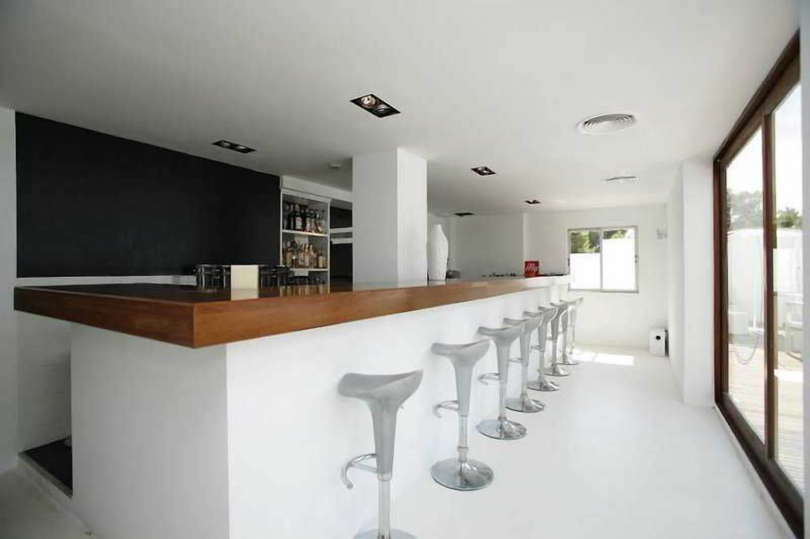 Un área de bar moderna con mostrador de madera y taburetes blancos.
