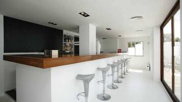 Un área de bar moderna con mostrador de madera y taburetes blancos.