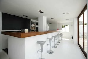 Un área de bar moderna con mostrador de madera y taburetes blancos.