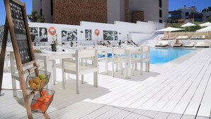 Ett område vid poolen med vita bord och stolar, en tavla där man kan skriva med krita och en stenmur i bakgrunden.
