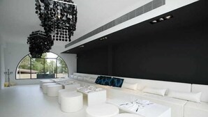 A modern interior with a long white sofa, multiple white round tables, and a unique black chandelier. - Hotel Zhero-palma (Calvia)