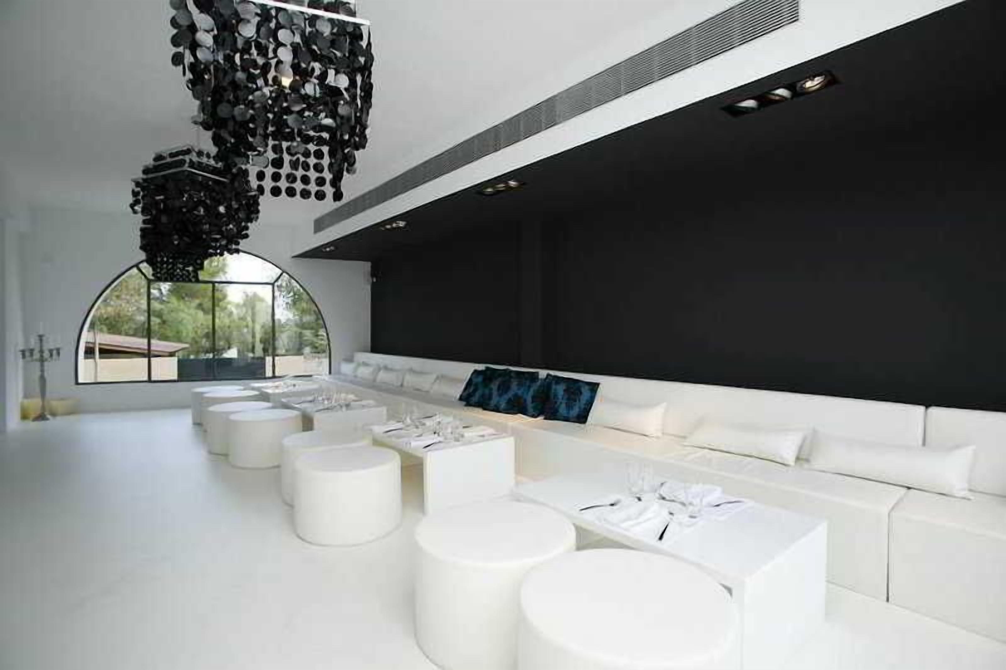 Un interior moderno con un sofá blanco largo, varias mesas redondas blancas y una lámpara de araña negra original.